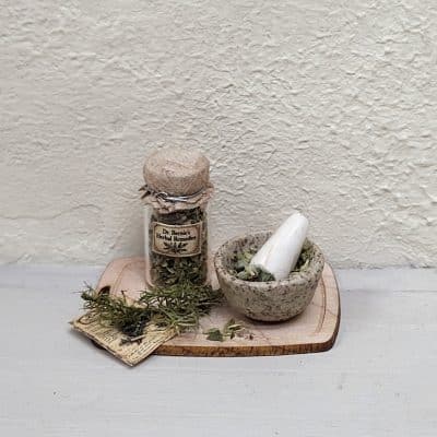 Handgemaakte kruidenapothekerset met glazen kruidenpotje, vijzel en gedroogde kruiden op een houten plankje, schaal 1:12.