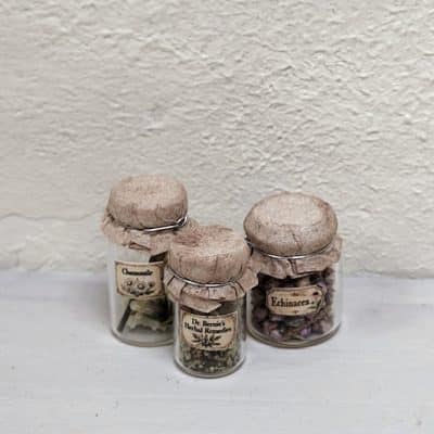Drie miniatuur kruidenpotjes met kurk, brocante papieren sluitingen en etiketten, gevuld met gedroogde kruiden en bloemen, schaal 1:12.